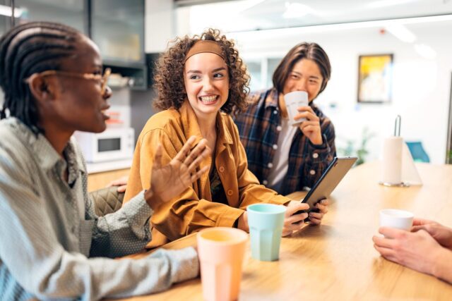 Gen Z und Boomer: Junge Frauen und ein dunkelhäutiger Mann sitzen an einem Tisch und unterhalten sich