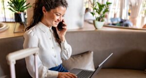 Routinen machen Geschäftsalltag flexibler Routinen machen Geschäftsalltag flexibel: Frau mit Trollen sitzt in einem Büro, hält ein Mobiltelefon ans Ohr und tippt auf dem Keyboard ihres Laptops