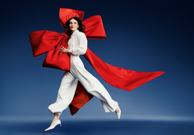 Flying Blue Eine Frau mit roter Schärpe hüpft vorm einem tiefblauen Hintergrund