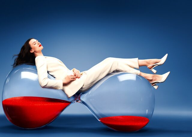 Air-France-Kampagne: Eleganz neu definiert: Eine Frau im weißen Hosenanzug liegt auf einer querliegenden Sanduhr mit roter Sand