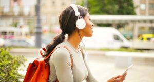 Wo allein reisende Frauen sicher sind: Solo-Travel 2026 Solo-Reisen: Spezifische Risiken für Frauen im Fokus: Junge Frau mit weißen Kopfhörer und rotem Rucksack sitzt uf einer Mauer und schaut auf den vorbeifahren Verkehr