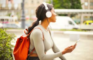 Wo allein reisende Frauen sicher sind: Solo-Travel 2026 Solo-Reisen: Spezifische Risiken für Frauen im Fokus: Junge Frau mit weißen Kopfhörer und rotem Rucksack sitzt uf einer Mauer und schaut auf den vorbeifahren Verkehr