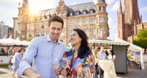Wiesbaden 2026: Kultur, Wein & Hollegha Ein Mann und ein Frau in ei9nem bunten Kleid Besuchern die Rheingauer Weinwoche in Wiesbaden