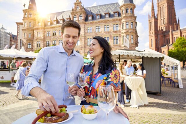 Ein Mann und ein Frau in ei9nem bunten Kleid Besuchern die Rheingauer Weinwoche in Wiesbaden