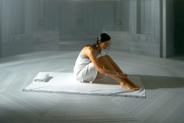 Wellness-Tourismus Türkei: Eine Frau sitzt in einem türkischen Dampfbad auf einer weißen Decken