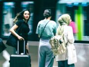 Travel Risk Awareness: 7 Risiken für Geschäftsreisen Travel Risk Awareness auf Geschäftsreisen: Junge Frau mit schwarzem Koffer, Bahnhof, vorbeifahrender Zug, zwei Reisende neben ihr