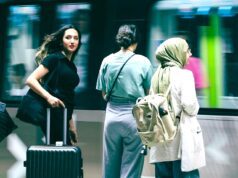 Travel Risk Awareness: 7 Risiken für Geschäftsreisen Travel Risk Awareness auf Geschäftsreisen: Junge Frau mit schwarzem Koffer, Bahnhof, vorbeifahrender Zug, zwei Reisende neben ihr