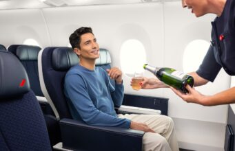 Air France erhöht das Reiseerlebnis in der Premium-Kabine Air France steigert das Reiseerlebnis in der Premium-Kabine: Ein sitzt im Flugzeug und eine Flugbegleiterin scheint ihm aus einer Flache Champagner ein