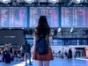Prägen Social Media Reiseentscheidungen? Social Media und Reiseentscheidungen: junge frau mit rucksack blickt auf eine große anzeigetafel mit abflügen in Flughafen
