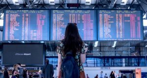 Prägen Social Media Reiseentscheidungen? Social Media und Reiseentscheidungen: junge frau mit rucksack blickt auf eine große anzeigetafel mit abflügen in Flughafen
