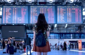 Prägen Social Media Reiseentscheidungen? Social Media und Reiseentscheidungen: junge frau mit rucksack blickt auf eine große anzeigetafel mit abflügen in Flughafen