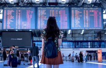 Prägen Social Media Reiseentscheidungen? Social Media und Reiseentscheidungen: junge frau mit rucksack blickt auf eine große anzeigetafel mit abflügen in Flughafen