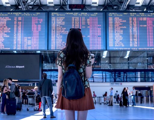 Prägen Social Media Reiseentscheidungen? Social Media und Reiseentscheidungen: junge frau mit rucksack blickt auf eine große anzeigetafel mit abflügen in Flughafen