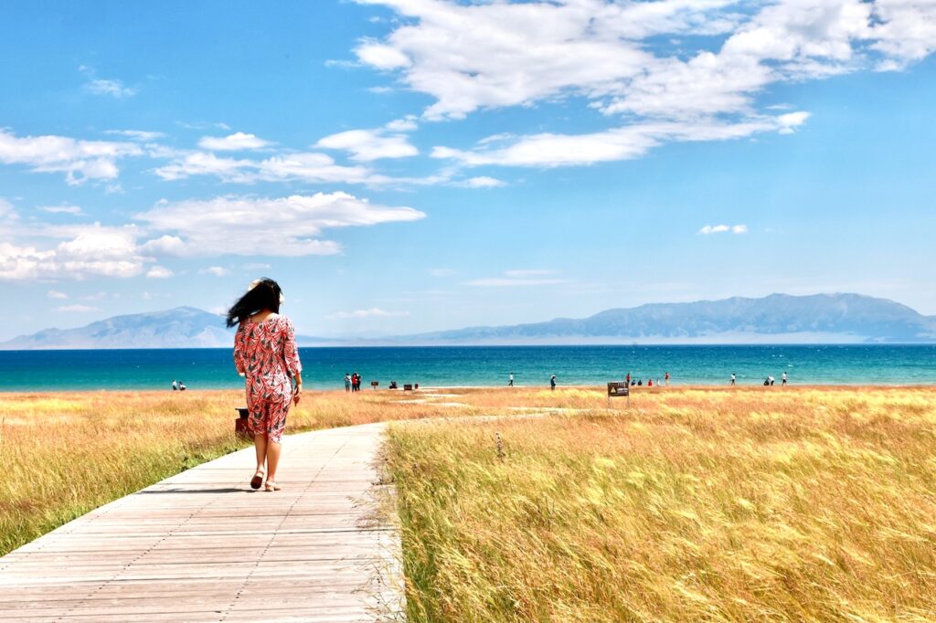 Eine Frau geht auf einem Weg zwischen gelben Feldern. Nachhaltig urlauben erfordert von allen Menschen bewusst reisen (Bild: Bingxiang Yan, Pixabay)
