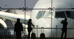 Geschäftsreisen: Die wichtigsten Key Insights Wie wichtig sind Geschäftsreisen wirklich? Eine Frau mit Handgepäck blickt von der Abflughalle durch einen großes Fenster auf ein Flugzeug