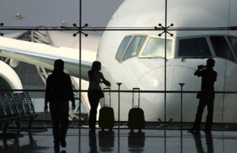 Geschäftsreisen: Die wichtigsten Key Insights Wie wichtig sind Geschäftsreisen wirklich? Eine Frau mit Handgepäck blickt von der Abflughalle durch einen großes Fenster auf ein Flugzeug