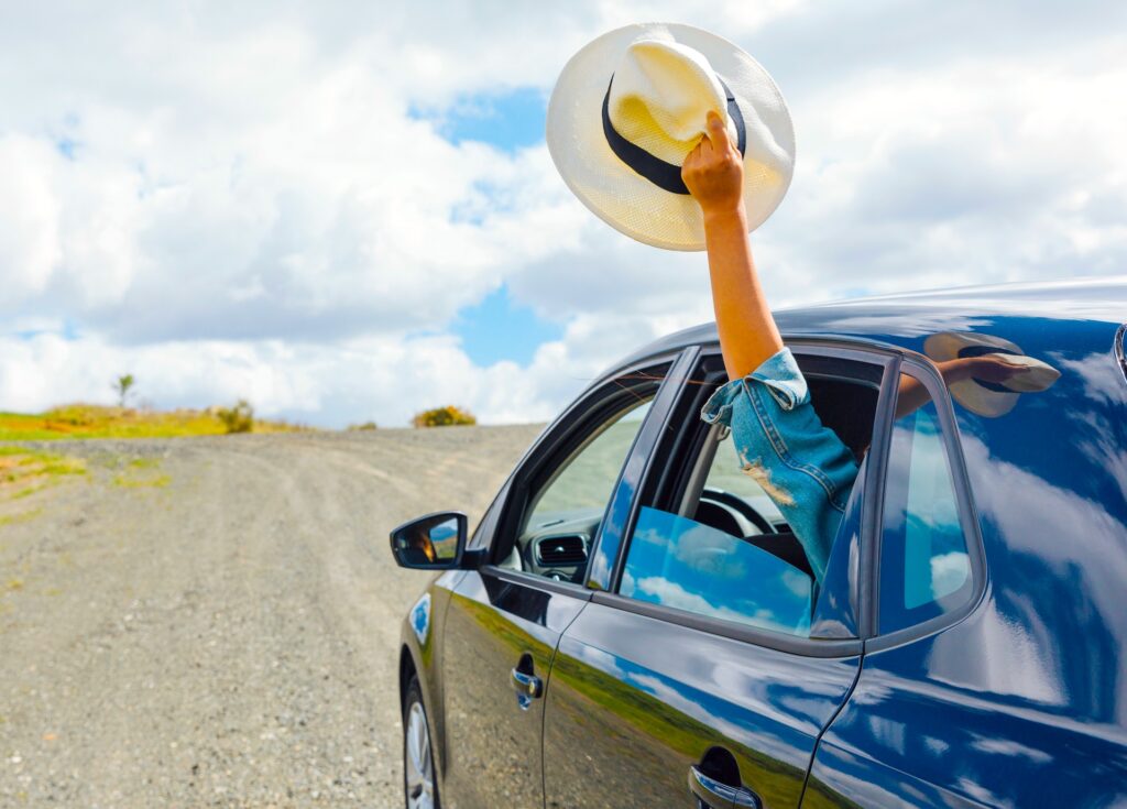 Österreicher lieben den Urlaub mit dem Auto: Frauenhand mit gelben Strohhut winkt aus dem Auto