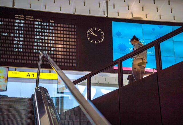 EU.Fluggastrechte gesichert: Anzeigetafel auf einem Flughafen, eine Person steigt eine Treppe herab