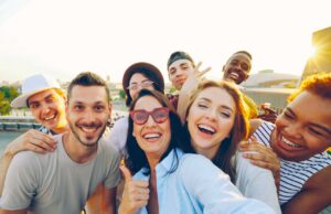 Kundenbindung im Tourismus neu gedacht Kundenbindung im Tourismus neu gedacht: Gruppe junger Männer und Frauen, die lachend den Fotografen anschauen und DAUMEN HOCHHEBEN
