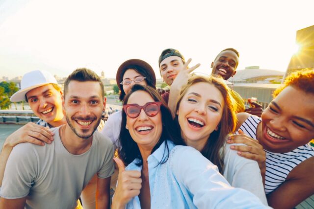 Kundenbindung im Tourismus neu gedacht Kundenbindung im Tourismus neu gedacht: Gruppe junger Männer und Frauen, die lachend den Fotografen anschauen und DAUMEN HOCHHEBEN