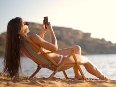 Im Urlaub für den Chef immer erreichbar? Im Urlaub: Frau im Liegestuhl mit Mobiltelefon in der Hand fotografiert Strand und Umgebung