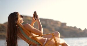 Im Urlaub für den Chef immer erreichbar? Im Urlaub: Frau im Liegestuhl mit Mobiltelefon in der Hand fotografiert Strand und Umgebung