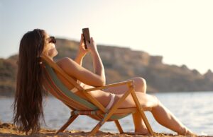 Im Urlaub für den Chef immer erreichbar? Im Urlaub: Frau im Liegestuhl mit Mobiltelefon in der Hand fotografiert Strand und Umgebung