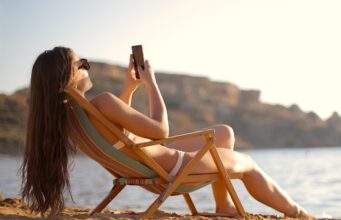 Im Urlaub für den Chef immer erreichbar? Im Urlaub: Frau im Liegestuhl mit Mobiltelefon in der Hand fotografiert Strand und Umgebung
