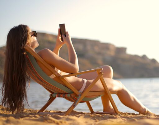 Im Urlaub für den Chef immer erreichbar? Im Urlaub: Frau im Liegestuhl mit Mobiltelefon in der Hand fotografiert Strand und Umgebung