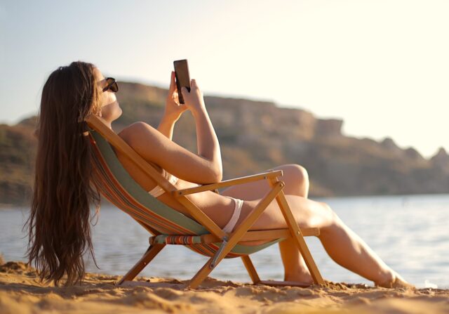 Im Urlaub immer erreichbar Im Urlaub: Frau im Liegestuhl mit Mobiltelefon in der Hand fotografiert Strand und Umgebung