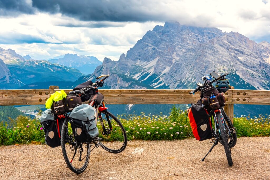 Legendäre Radtouren in der Welt der Berge: Zwei Bikepacking-Räder auf einem Weg mit Blick auf eine Gipfel und Wolken am Himmel