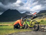 Legendäre Radtouren von Island bis Südkorea Legendäre Radtouren: Radfahrer stellt das Gang bei einem beladenen Fahrrad in der rauen Landschaft Islands unter dramatischen Himmel ein.