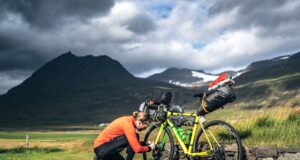Legendäre Radtouren von Island bis Südkorea Legendäre Radtouren: Radfahrer stellt das Gang bei einem beladenen Fahrrad in der rauen Landschaft Islands unter dramatischen Himmel ein.