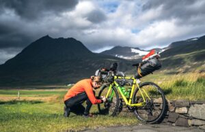 Legendäre Radtouren von Island bis Südkorea Legendäre Radtouren: Radfahrer stellt das Gang bei einem beladenen Fahrrad in der rauen Landschaft Islands unter dramatischen Himmel ein.