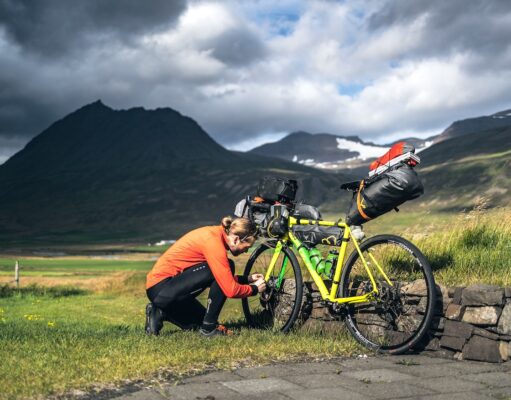 Legendäre Radtouren von Island bis Südkorea Legendäre Radtouren: Radfahrer stellt das Gang bei einem beladenen Fahrrad in der rauen Landschaft Islands unter dramatischen Himmel ein.