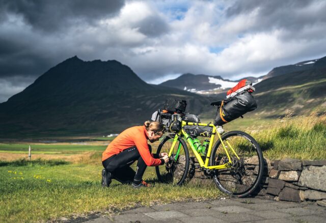Legendäre Radtouren: Radfahrer stellt das Gang bei einem beladenen Fahrrad in der rauen Landschaft Islands unter dramatischen Himmel ein.