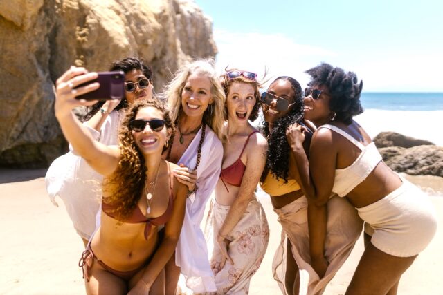 Social Media im Tourismus Social Media im Tourismus schlägt Wellen: Junge Gruppe von Frauen macht Selfies am Strand