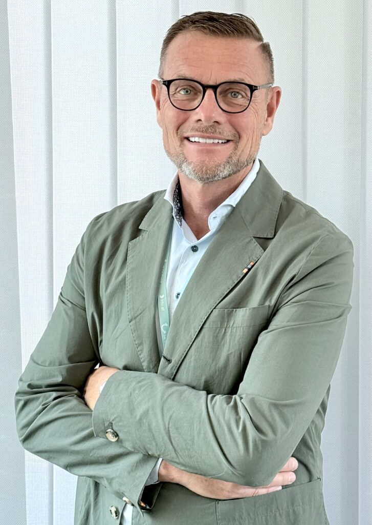 Im Bild ein bebrillter Mann in einem grünen Sakko mit verschränkten Armen: BTU-Co-CEO Hubert Kluske