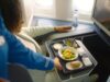 Das neue Bordservice: Grand Café KLM Bordservice Gand Café KLM: Frau sitzt im Flugzeug, vor ihr ein Tablett mit diversen Speisen