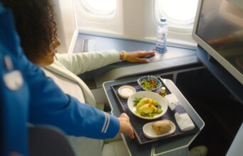 Das neue Bordservice: Grand Café KLM Bordservice Gand Café KLM: Frau sitzt im Flugzeug, vor ihr ein Tablett mit diversen Speisen