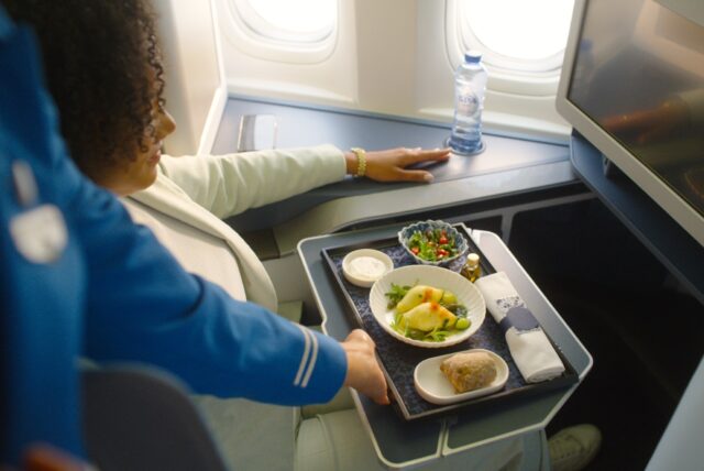 KLM Bordservice Grand Café KLM 1920_cateringaiklm Bordservice Gand Café KLM: Frau sitzt im Flugzeug, vor ihr ein Tablett mit diversen Speisen