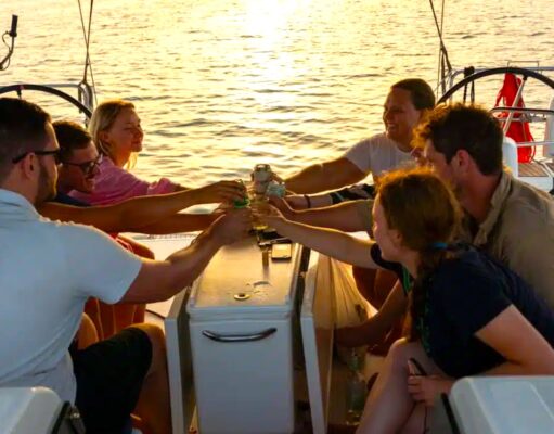 Kojencharter: Segelurlaub für neue Zielgruppen Kojencharter: Segelurlaub für neue Zielgruppen: Vier Personen sitzen in einem Segelboot, im Higergrund spiegelt sich die Sonne im Meer