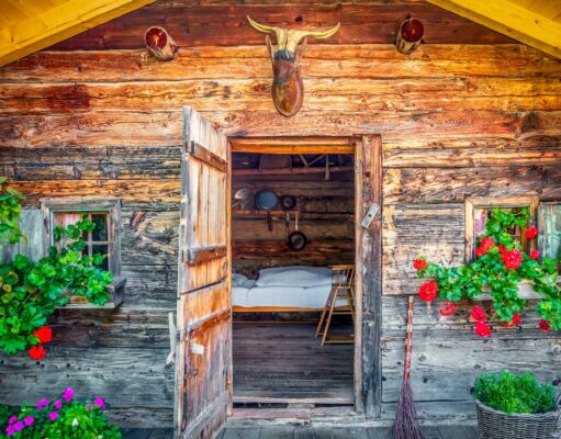 Almhütten: So werden Bettwanzen gestoppt! Almhütten und die Bettwanzen: Eine alpine Hütte mit geöffneter Tür und Blick auf ein ein weiß getünchtes Bett