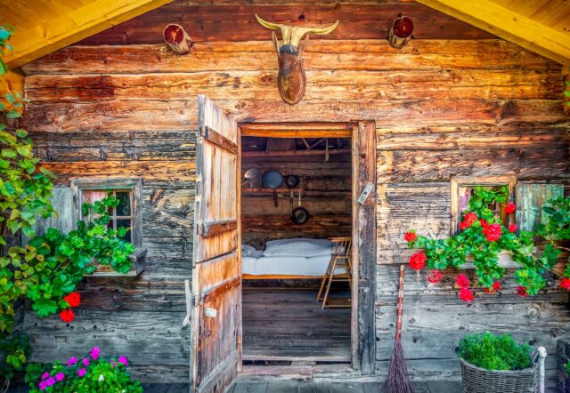 Almosen und Bettwanzen Almhütten und die Bettwanzen: Eine alpine Hütte mit geöffneter Tür und Blick auf ein ein weiß getünchtes Bett