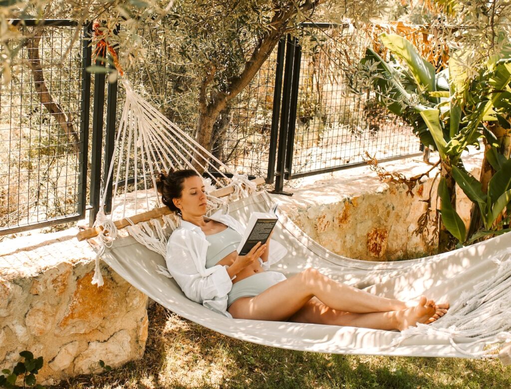 Work-Life-Balance: Eine Frau im Bikini liegt in einer Hängematte in einem Garten und liest ein Buch