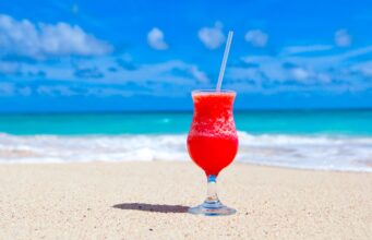 Karibik-Regionalnetz der Air France erweitert Karibik-Regionalnetz der Air France erweitert: Willkommen in Übersee. Auf weißem Sandstrand, im Hintergrund das blaue Meer und der blauen Himmel, steht ein Glas mit pinken Getränk und Strohhalm