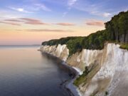 KI-Anwendung der DZT gewinnt Auszeichnung Eine Küstenlandschaft mit weißen Kreidefelsen entlang der Küstenlinie der Ostsee in Rügen und einem dichten Buchenwald im Nationalpark Jasmund darüber.