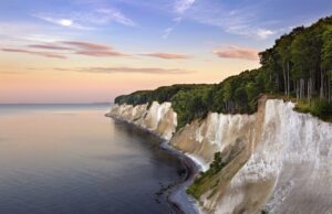 KI-Anwendung der DZT gewinnt Auszeichnung Eine Küstenlandschaft mit weißen Kreidefelsen entlang der Küstenlinie der Ostsee in Rügen und einem dichten Buchenwald im Nationalpark Jasmund darüber.