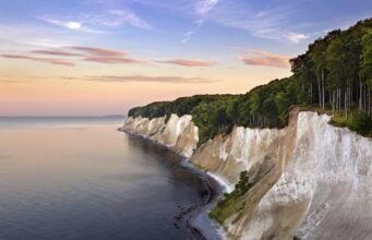 KI-Anwendung der DZT gewinnt Auszeichnung Eine Küstenlandschaft mit weißen Kreidefelsen entlang der Küstenlinie der Ostsee in Rügen und einem dichten Buchenwald im Nationalpark Jasmund darüber.