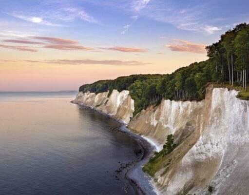 KI-Anwendung der DZT gewinnt Auszeichnung Eine Küstenlandschaft mit weißen Kreidefelsen entlang der Küstenlinie der Ostsee in Rügen und einem dichten Buchenwald im Nationalpark Jasmund darüber.